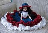 a doll sitting on top of a couch wearing a red and blue dress with ruffles