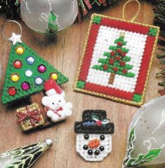 cross stitch christmas ornaments on a wooden table next to a tree and snowman ornament