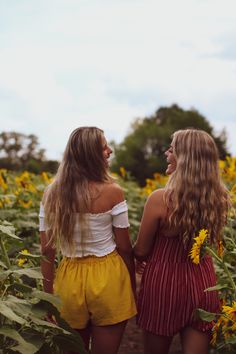 two young women walking through a field of sunflowers with their backs to each other