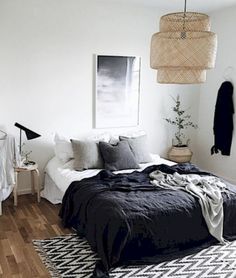 a bedroom with black and white bedding, wooden flooring and hanging lights above the bed