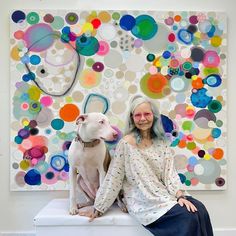 a woman sitting next to a dog in front of a colorful wall with circles on it