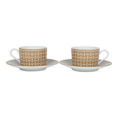 two coffee cups and saucers with gold designs on them, one is white and the other is brown