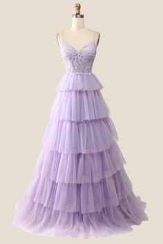 This lilac gown features a tulle material and a playful A-line silhouette. The lace corset bodice has double straps, while the tiered ruffle length skirt adds a touch of whimsy. Don't forget the lace-up back for a perfect fit! Lavender Prom Dress With Ruffles, Lavender Ruffled Dress For Wedding, Lavender Tulle Dress With Ruffles, Purple Tulle Dress With Ruffles, Purple Ruffled Ball Gown For Wedding, Tulle Gown With Fitted Bodice And Tiered Shape, Tiered Gown For Prom Season, Purple Sleeveless Ruffled Gown, Lavender Ruffled Wedding Gown