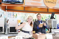 a man and woman standing in front of a counter holding up beer glasses while smiling at the camera