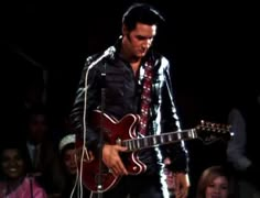 a man with a red guitar standing in front of a microphone and some other people