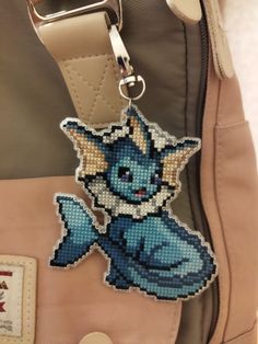 a cross stitch keychain hanging from a handbag with an image of a pokemon character on it