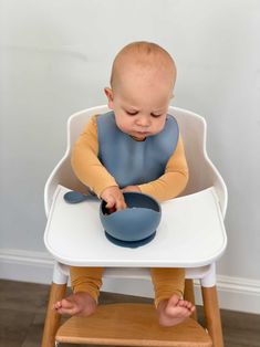 a small child sitting in a high chair eating from a blue bowl on top of it