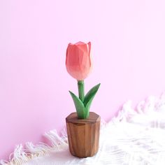 a single pink tulip in a wooden vase on a white blanket against a pink wall