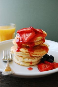 a stack of pancakes with strawberries and syrup on a plate next to a glass of orange juice