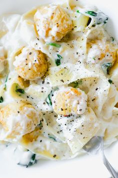 a white plate topped with pasta and meatballs covered in cheese sauce next to a fork