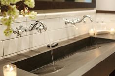 a bathroom sink with two faucets and candles on the counter next to it