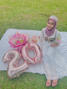 a woman sitting on a blanket with some balloons and flowers in front of her, next to the number 20