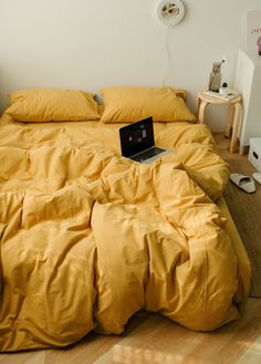 an open laptop computer sitting on top of a yellow comforter in a bed room