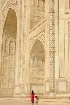 two people walking in front of an intricately carved building with arches and doorways