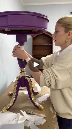 a woman is working on a table with purple paint and gold trimming around it