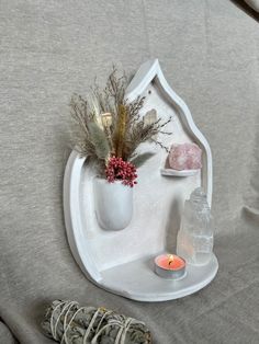 a white shelf with some flowers and candles on it next to a candle holder that is shaped like a house