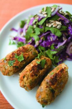 some food is on a white plate next to a purple cabbage and green leafy salad