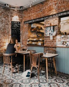 two people are sitting at tables in a small restaurant with brick walls and flooring