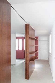 an empty room with wooden shelves and white walls, along with a red door that leads to another room