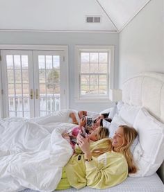 two women laying on a bed with white sheets