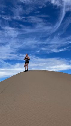 a woman standing on top of a sand dune under a blue sky with wispy clouds