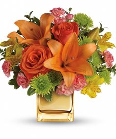 an orange and yellow bouquet in a square vase on a white background with green accents