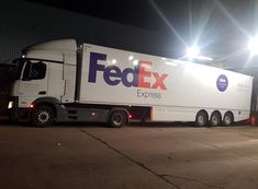 a fedex truck parked in front of a building at night with its lights on