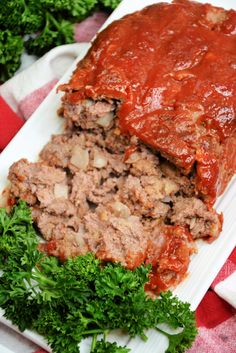 meatloaf with sauce and parsley on a white platter, ready to be eaten