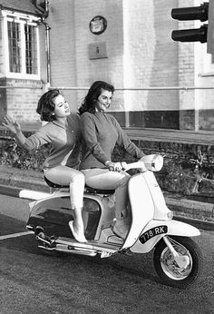 two women riding on the back of a scooter