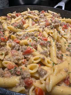 a skillet filled with pasta, meat and vegetables on top of a stovetop