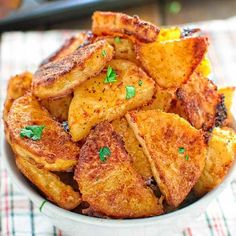 a white bowl filled with fried potatoes on top of a checkered cloth next to a fork