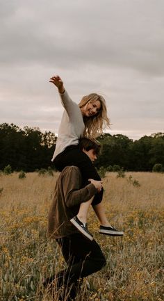 two people are in the middle of a field with tall grass and trees behind them