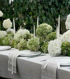 there are many white flowers and candles on the table with place settings in front of them