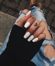 a person with white nails and a crescent moon tattoo on their finger is sitting down