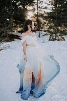 a woman standing in the snow wearing a white dress with an orange and blue skirt