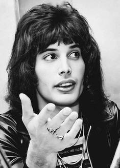 a black and white photo of a woman holding her hand up to the side while wearing a leather jacket