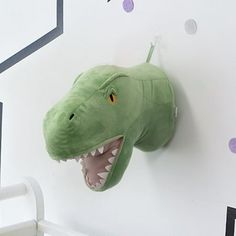 a stuffed dinosaur head mounted to the side of a white wall next to a crib