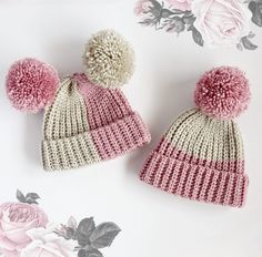 two knitted beanies with pom - poms on them next to flowers