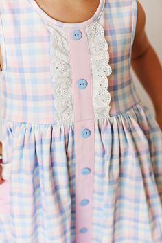 This beautiful dress features a soft pastel gingham check print, trimmed eyelet bib and pockets, paired with sweet little blue buttons. Pre-Order item only: This item is for pre-order. Secure your size by placing a pre-order for this item. We will ship your items promptly when they arrive at our shop. Our orders were placed this past year and all styles/sizes you see under pre-order should arrive to our shop in the next 2-3 weeks. Please allow 2-3 weeks for all pre-order items. If there are any delays, we will contact you directly. If you are purchasing multiple items with your pre-order, please be aware we will bundle your items and ship complete. Style: 2450 Material: 95% cotton 5% spandex Sizing: Serendipity Clothing fits true to size. If you have any questions or need a measurement, pl Cute Cotton Plaid Dress For Spring, Cute Plaid Cotton Dress For Spring, Summer Gingham Dresses With Pockets, Cotton Gingham Dress With Lace Trim, Cotton Buttoned Dress For Picnic, Gingham Cotton Dress With Lace Trim, Picnic Gingham Dress With Lace Trim, Cotton Dresses With Buttons For Picnic, Cotton Lace Trim Dress For Picnic