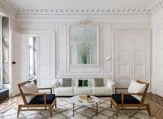 a living room with white walls and wooden floors, two chairs and a coffee table