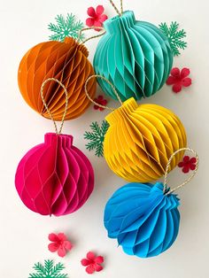 three colorful paper lanterns hanging from string on white surface with red and green flowers in the background