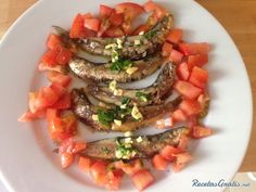 there is a white plate with some fish and tomatoes on it, ready to be eaten