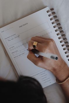 a person writing in a notebook with a pen on top of the page and another hand holding a pencil