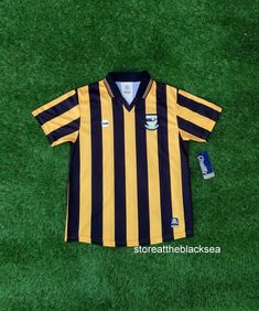 a yellow and black striped soccer jersey laying on the grass with a bottle of beer