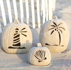 three carved pumpkins sitting in the sand with designs on them and one has a lighthouse