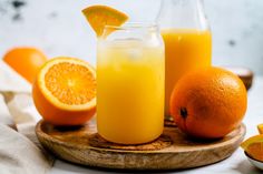 an orange juice in a glass next to some sliced oranges on a cutting board