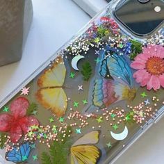 a phone case with butterflies and flowers on it sitting next to a vase filled with flowers