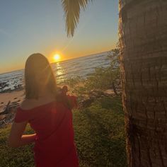 a woman standing next to a palm tree on top of a lush green field near the ocean