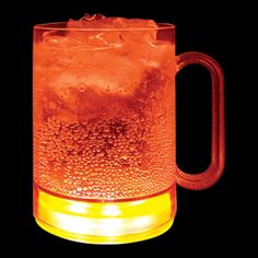 a glass mug filled with ice and water on top of a black surface, lit up by a yellow light