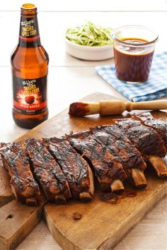 ribs on a cutting board next to a bottle of beer and other foodstuffs